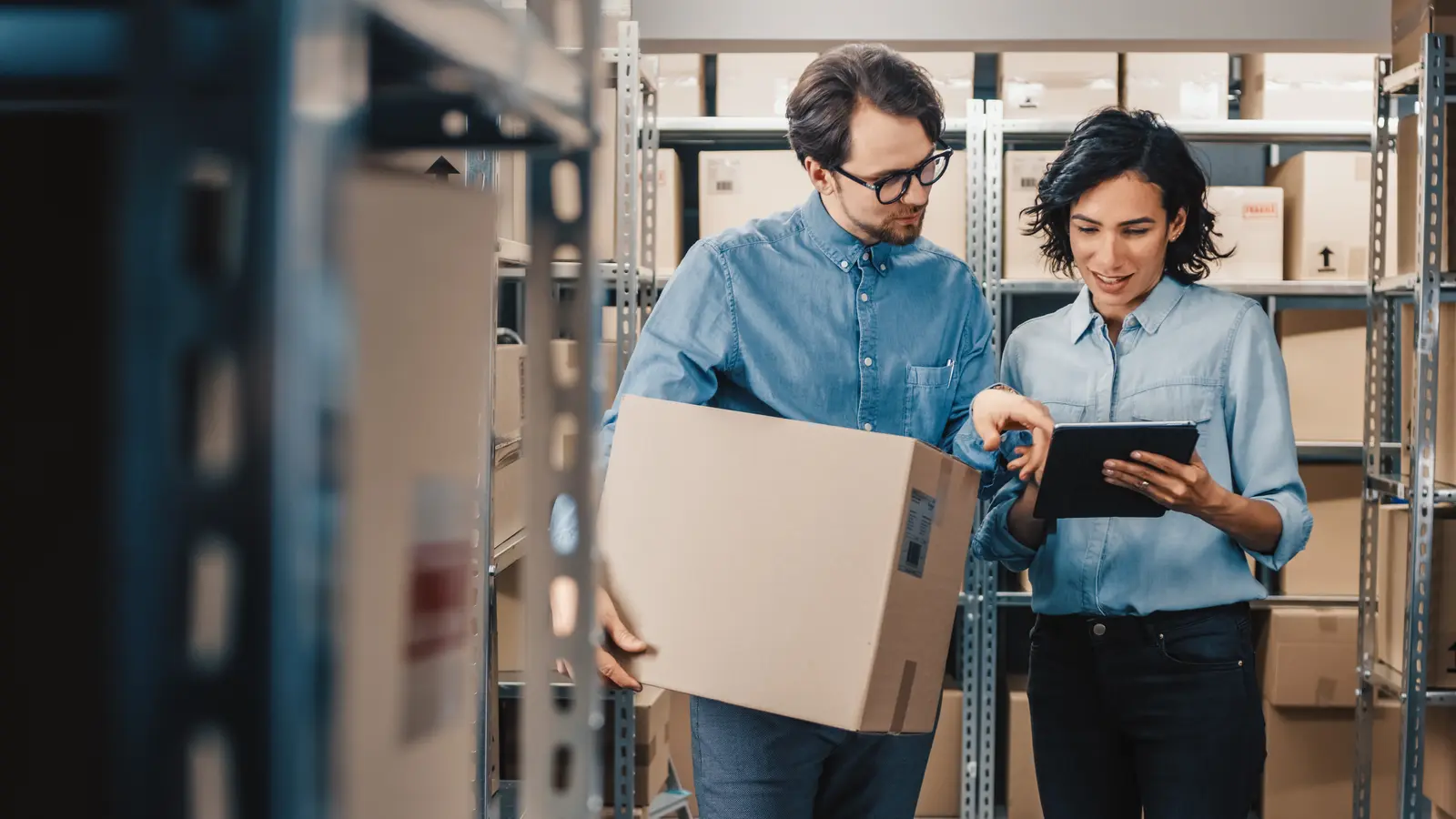 Employé logistique préparant soigneusement des produits fragiles dans une grande caisse en carton.
